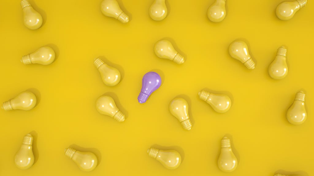 Standout purple light bulb among yellow bulbs on a yellow surface symbolizing individuality.
